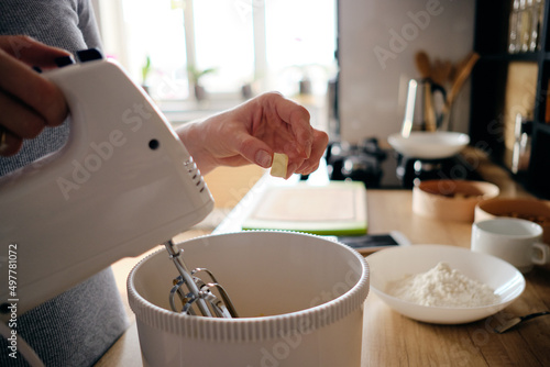 Woman hands baking a gem pie in the kitchen standing at the counter using a handheld mixer to whisk freshest ingredients in a white mixing bowl, ingredients on the table