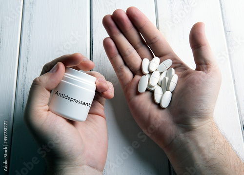 white pills and a jar with inscription antidepressant in human hand on a wooden table photo