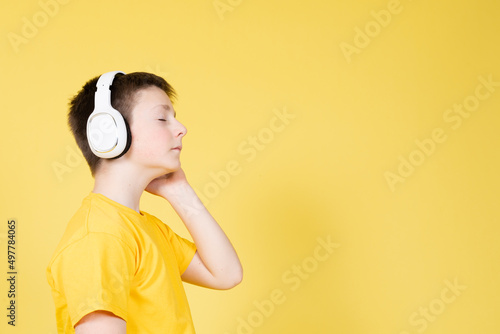 Side view of boy listening relaxing music on headphones with closed eyes isolated on yellow background with copy space