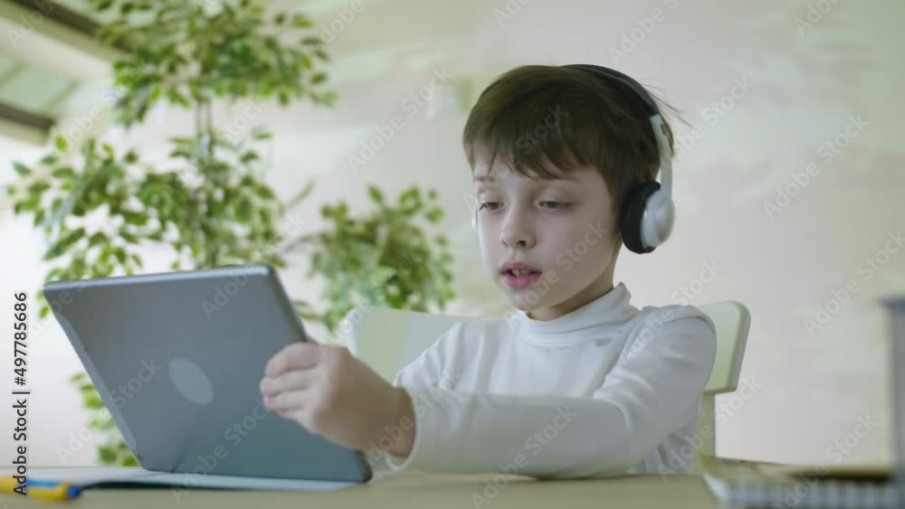 Curious Child Little school Boy Using Digital Tablet Technology Device Sitting At The Table Listening To Music Surfing Internet Play Game At Home Children Tech Addiction Concept Curious Child Little school Boy Using Digital Tablet Technology Device Sitting At The Table Listening To Music Surfing Internet Play Game At Home Children Tech Addiction Concept