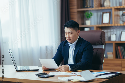 Accountant-auditor works in a classic office, calculates financial reports, Asian businessman works with computer and documents, paperwork