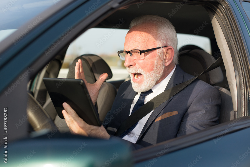 Angry senior businessman using digital tablet in the car Angry senior businessman using digital tablet in the car