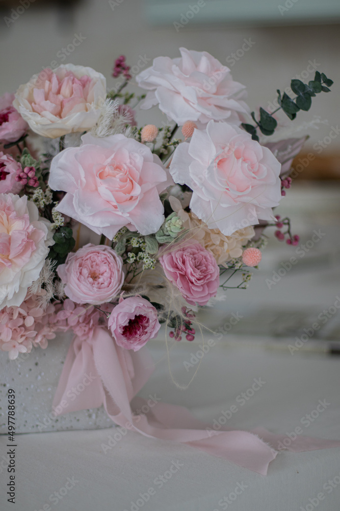 Beautiful bouquet of peonies and pink roses on the table. In the background is the interior of a modern white kitchen. Concept of home comfort.