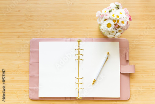 Flat lay, top view of a pastel pink diary flower bouquet and stationery on a wooden desk.