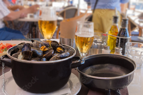 Cooked mussels in garlic sauce in a black saucepan on a table in a fish restaurant. Delicious lunch with seafood and beer. Gastronomic travel. Close-up