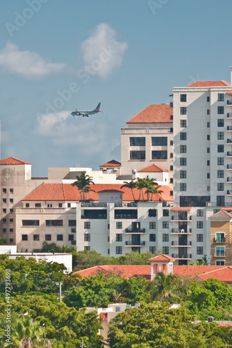 front view, far distance of a commercial, passenger jet landing at a tropical airport, surrounded by condominium buildings on a sunny afternoon