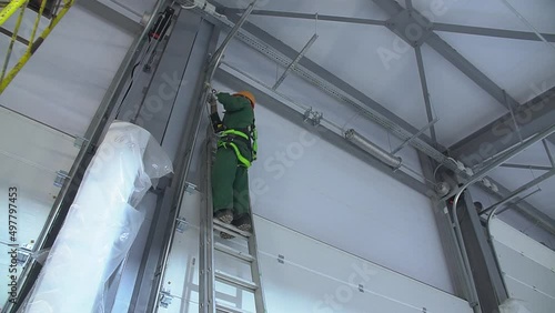 Professional worker climbing up ladder indoors to repair a transformer. Man in a workwear