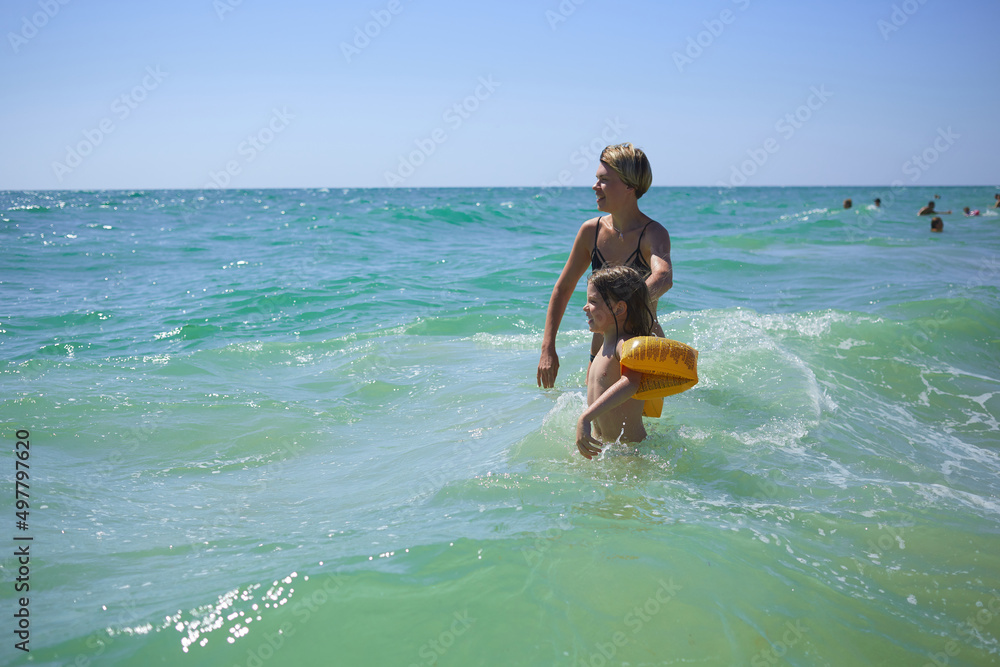 Summer happy family of six years blonde child playing and jumping water waves embracing woman mother in sea shore beach Summer happy family of six years blonde child playing and jumping water waves embracing woman mother in sea shore beach