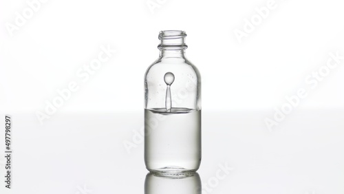 Drop of hyaluronic acid falls down into medical bottle with grey transparent liquid making column splash inside it on white background | Abstract cosmetics formulating concept photo