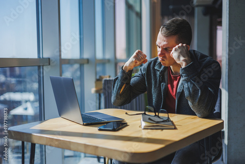 Portrait of a man, IT professional, working remotely with a modern laptop, sitting at a table and smiling at the camera during a break, a happy human programmer in vision correction glasses