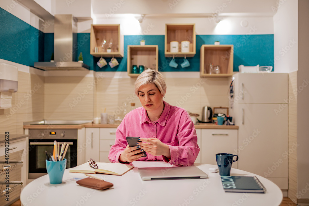 Short haired woman using smartphone in the kitchen at home Short haired woman using smartphone in the kitchen at home