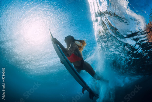 Slim surfer girl with surfboard dive underwater with under ocean wave.
