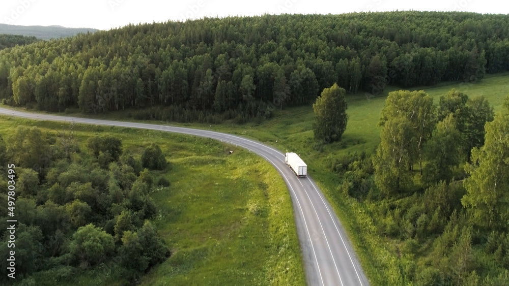 Bird's-eye view.Scene.A large green forest next to the road on which a large white truck is driving next to a green clearing.