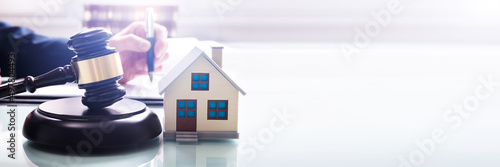 House Model With Gavel In Front Of A Businessperson