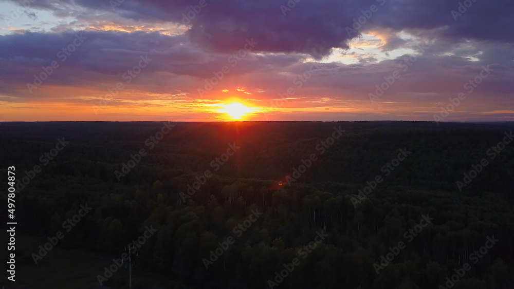 Spectacular sky from a drone. Clip. A beautiful bright sunset with purple and orange shades, where the sun can be seen over the forest