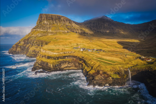 Sunny view of Mulafossur waterfall with Gasadalur village on background. Vagar island, Faroe Islands, Denmark. November 2021. Lonf exposure picture