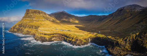 Sunny view of Mulafossur waterfall with Gasadalur village on background. Vagar island, Faroe Islands, Denmark. November 2021. Lonf exposure picture photo