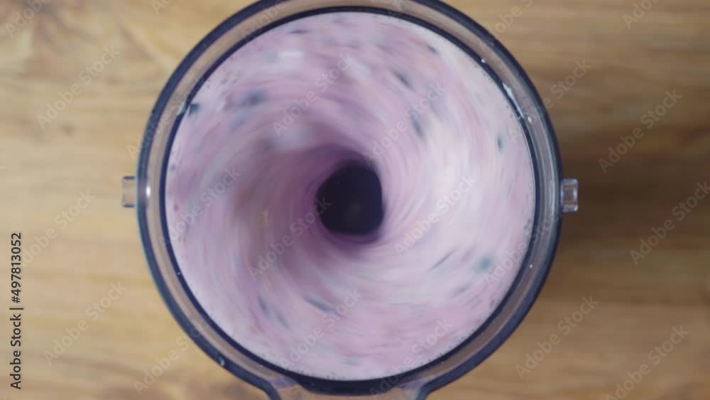 Running blender mixing raw blueberries and fresh milk, making a healthy delicious shake, top down view. Running blender mixing raw blueberries and fresh milk, making a healthy delicious shake, top down view.