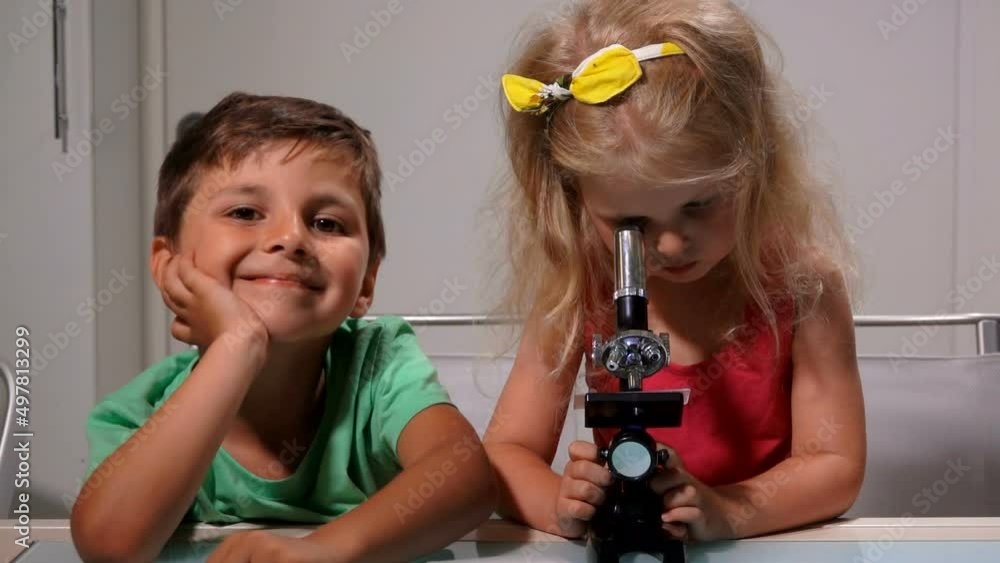 Cute little girl and boy are looking through a microscope lense Cute little girl and boy are looking through a microscope lense