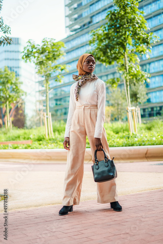 Confident black woman in trendy outfit and hijab holding bag