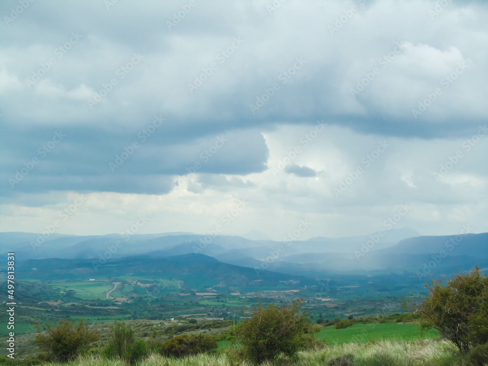 Landscape of green plains with a cloudy sky over distant mountains