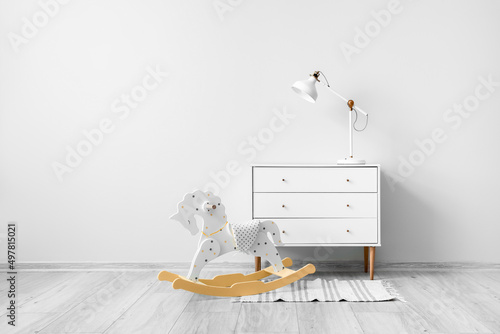 Chest of drawers with lamp and rocking horse near light wall photo