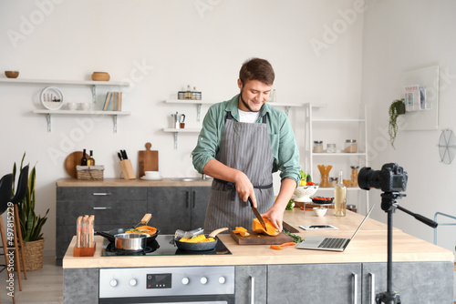 Young man cutting squash while following video tutorial in kitchen