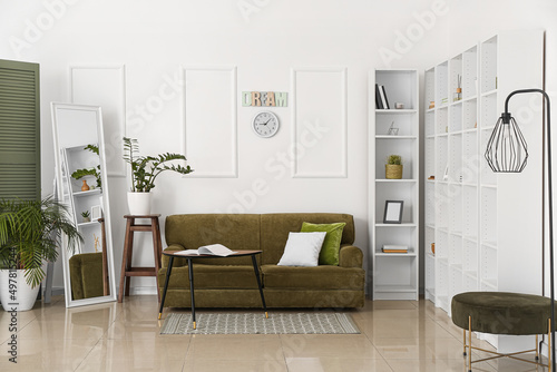 Interior of room with comfortable sofa  mirror and shelf unit near light wall