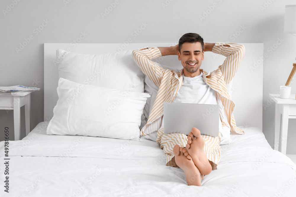 Young barefooted man using laptop in bedroom Young barefooted man using laptop in bedroom