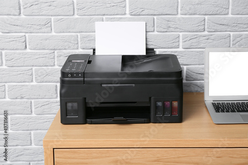 Workplace with modern laptop and printer near grey brick wall, closeup