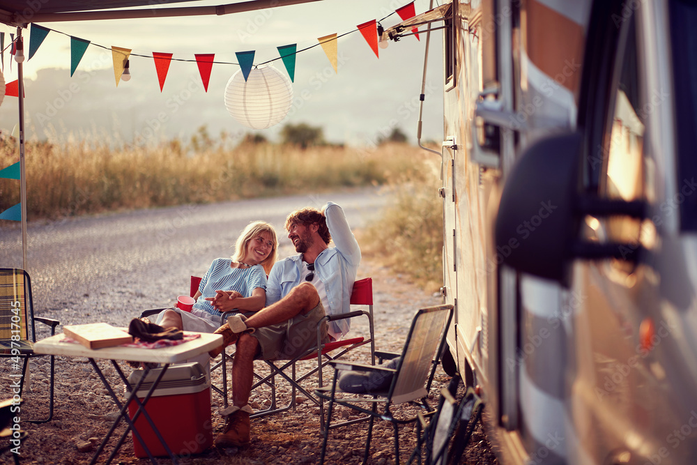 © luckybusiness - Couple in love, sitting and smilling at each other in front of camper rv. Fun, travel, togetherness, lifestyle, love concept.