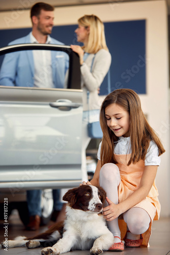 Young girl cuddling dog while mother bying a new car photo
