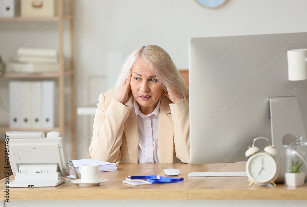 Stressed mature secretary at table in office Stressed mature secretary at table in office