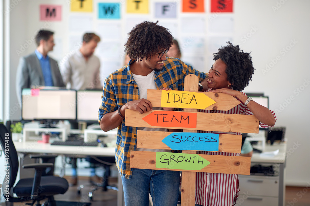 Young cheerful colleagues are holding a sign with company slogans and ...