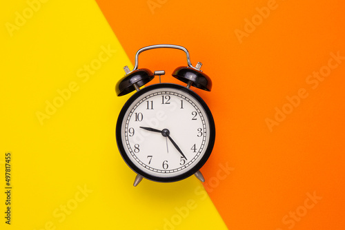 black alarm clock on yellow orange background. Minimalism concept