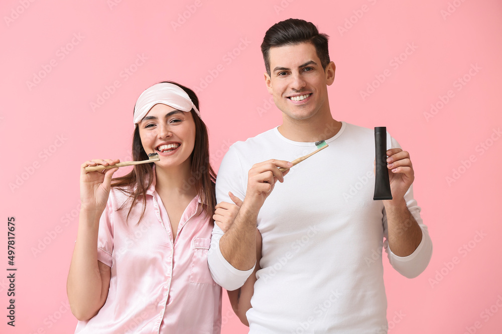 Young couple brushing teeth with activated charcoal tooth paste on pink background