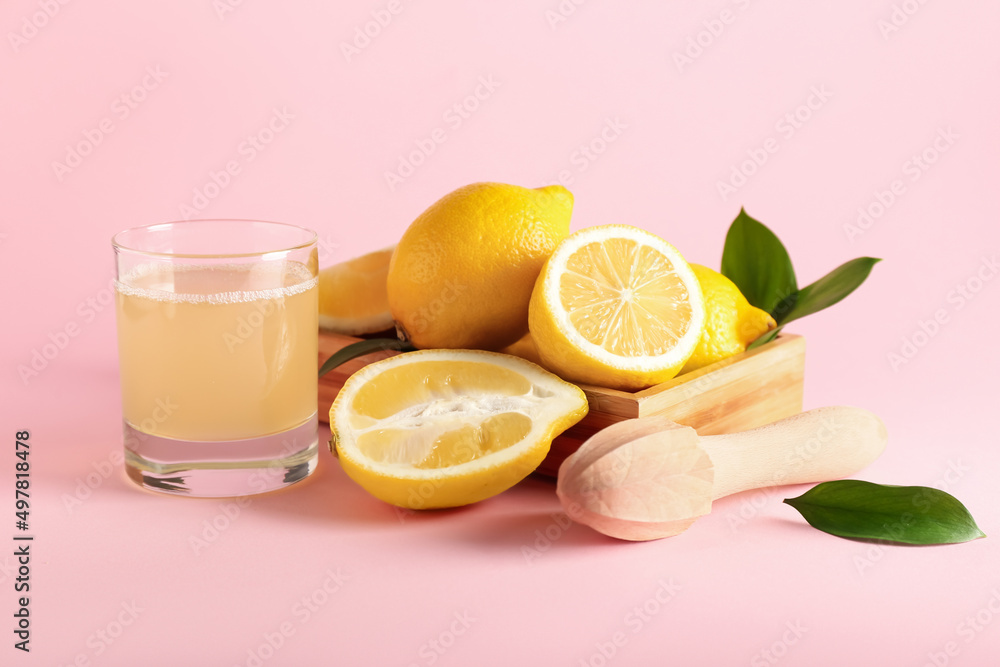 Wooden box with ripe lemons, juicer and glass of juice on pink background Wooden box with ripe lemons, juicer and glass of juice on pink background