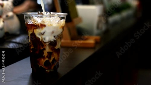 Barista pouring milk into a glass of iced coffee