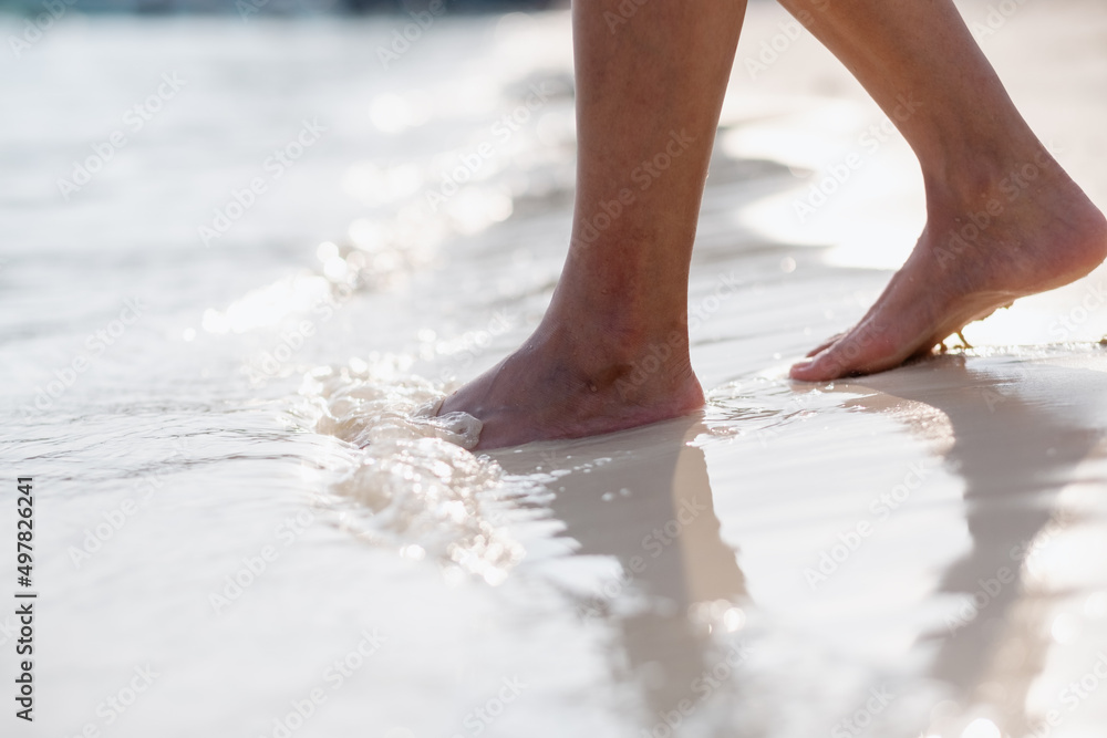 Closeup image of woman with barefoot while walking on the white beach and the sea Closeup image of woman with barefoot while walking on the white beach and the sea