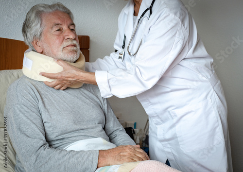 Senior bearded man in pain wearing a cervical collar with the assistance of a physiotherapist doctor during a visit home photo