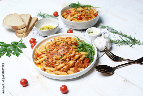 Italian pasta penne tomato sauce in white plate and breads with garlic oil on the white wood table.