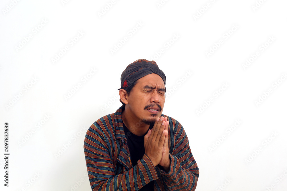 Sad asian man in java traditional costume begging for forgiveness. Isolated on white background Sad asian man in java traditional costume begging for forgiveness. Isolated on white background
