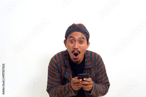 Wow and shocked face of Asian man in java traditional costume while looking at his cellular phone. © SetianingDyah