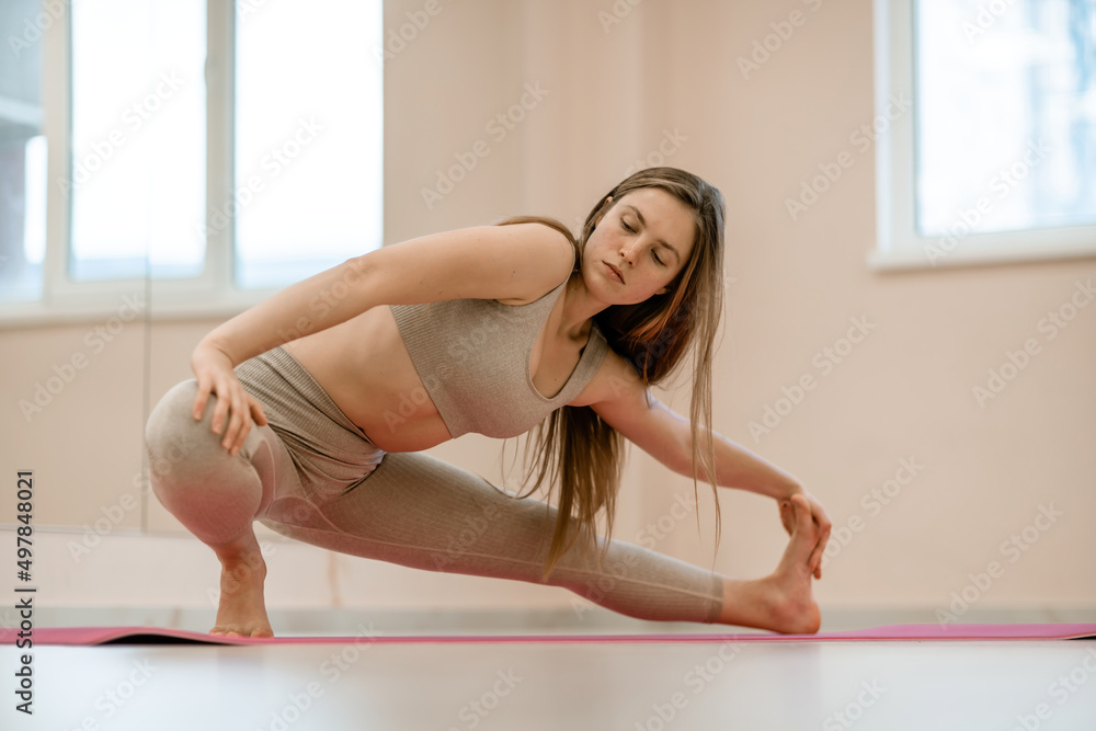 Fototapeta premium Girl does yoga. Young woman practices asanas on a beige one ton background.