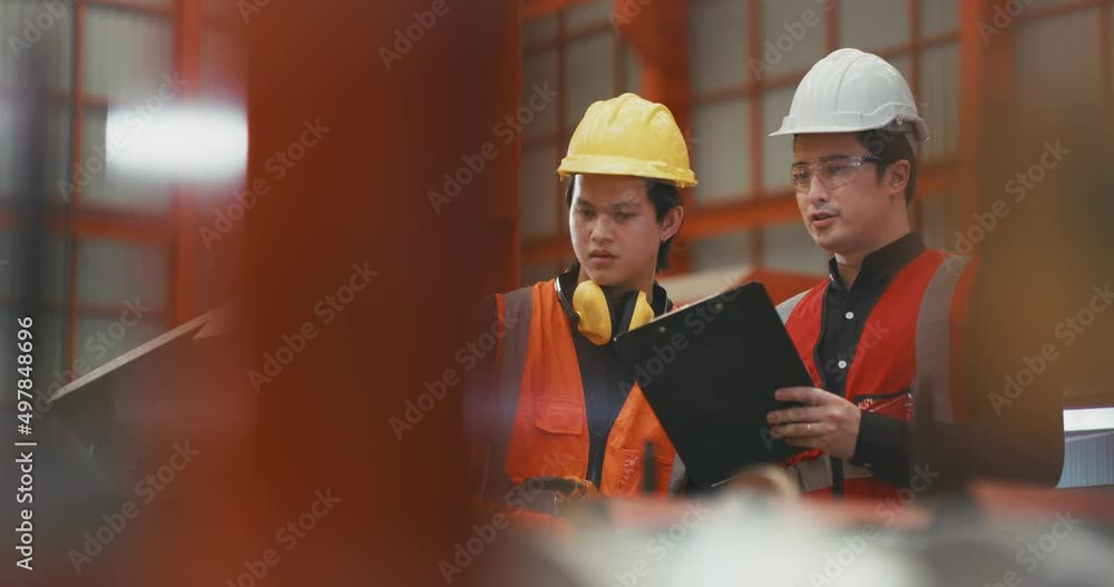 Two workers wearing hardhats, looking clip board Two workers wearing hardhats, looking clip board