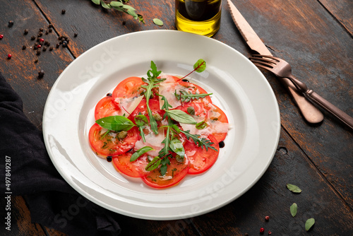 Light Salad with thinly sliced tomatoes, arugula, parmesan, capers and balsamic sauce. Vegetarian tomato salad on wooden table