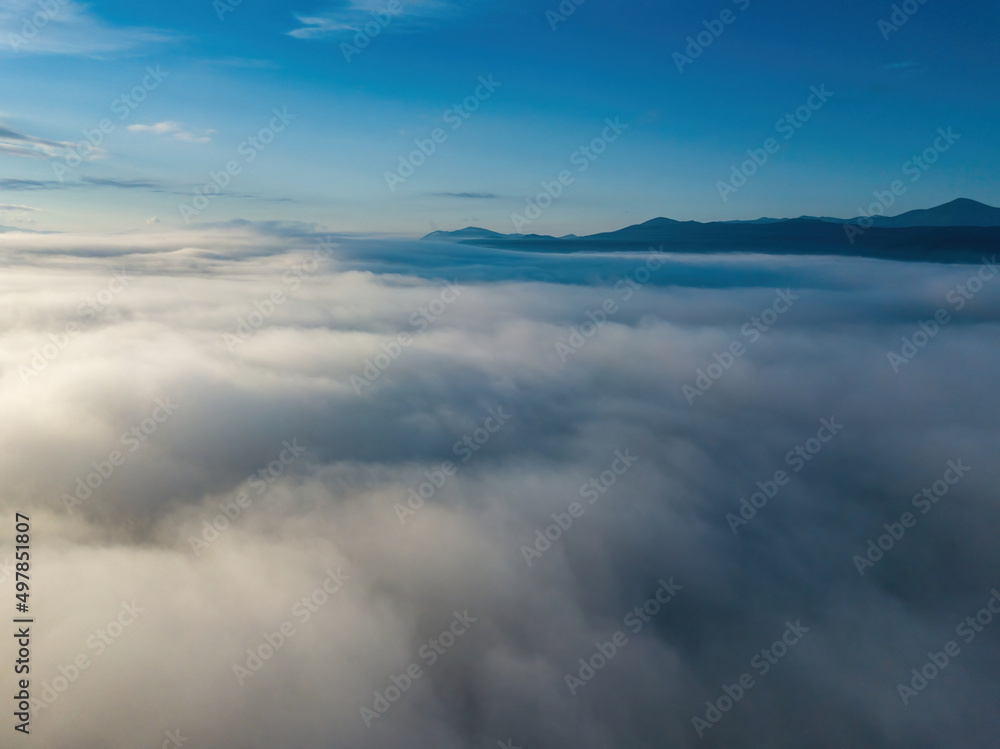 Flight over fog in Ukrainian Carpathians in summer. A thick layer of fog covers the mountains with a solid carpet. Mountains on the horizon. Aerial drone view.