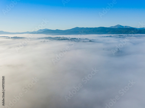 Flight over fog in Ukrainian Carpathians in summer. Mountains on the horizon. A thick layer of fog covers the mountains with a continuous carpet. Aerial drone view.