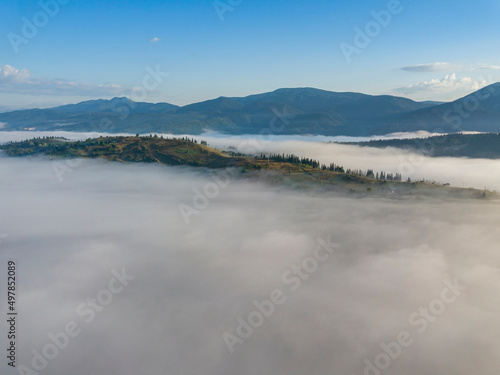 Flight over fog in Ukrainian Carpathians in summer. Mountains on the horizon. A thick layer of fog covers the mountains with a continuous carpet. Aerial drone view.