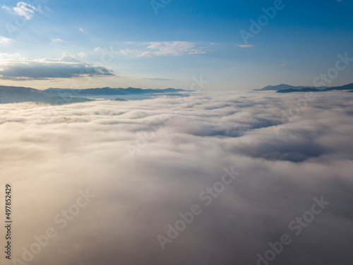 Flight over fog in Ukrainian Carpathians in summer. Mountains on the horizon. A thick layer of fog covers the mountains with a continuous carpet. Aerial drone view.